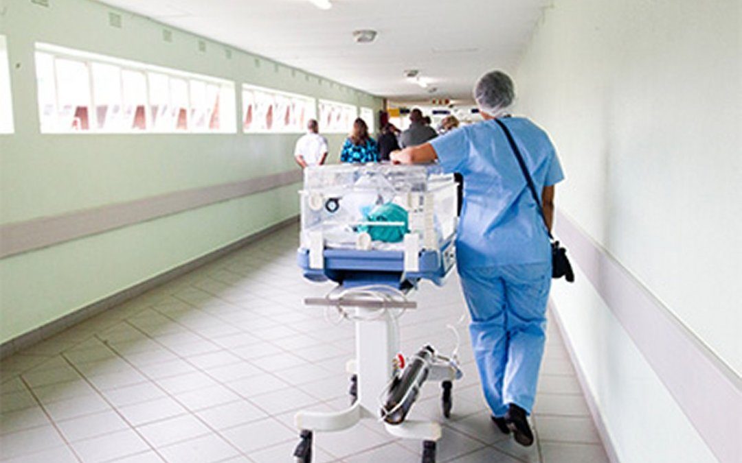 Healthcare worker walking down hospital hallway while pushing gurney