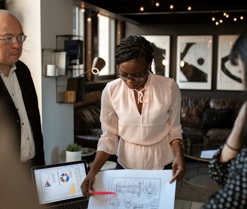 Black woman reviewing plans while standing at a conference table with two others.