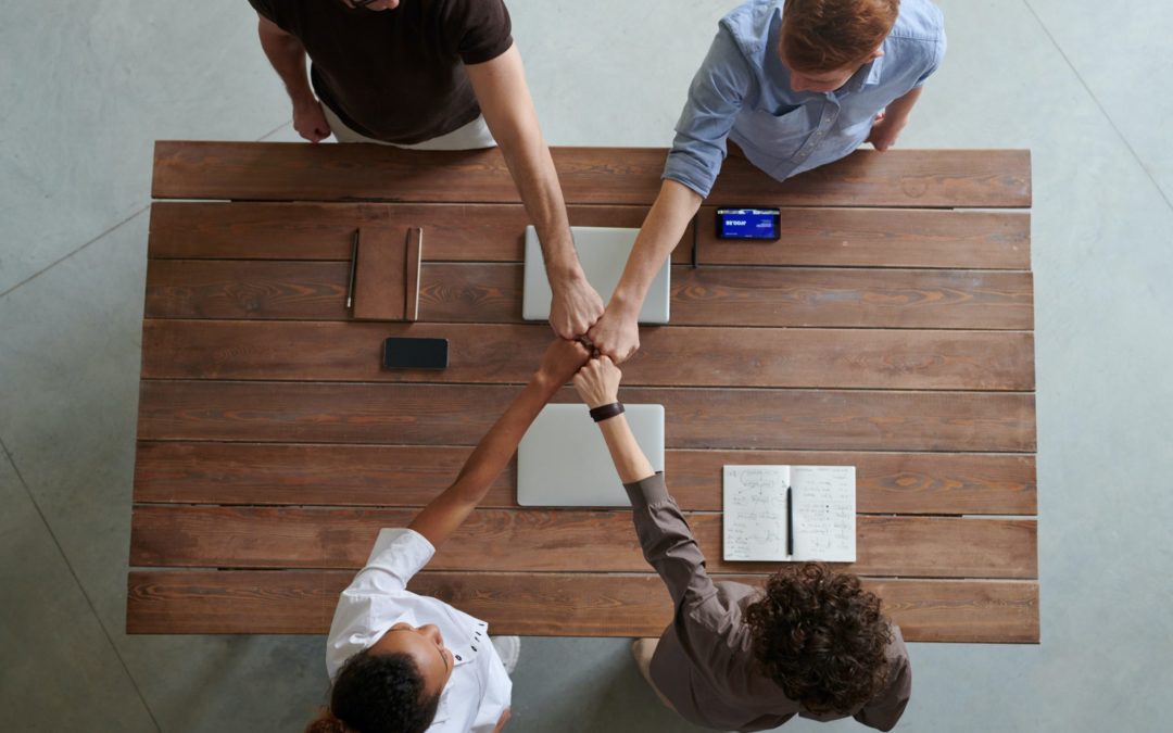 Four people sitting at a table doing a fist bump.